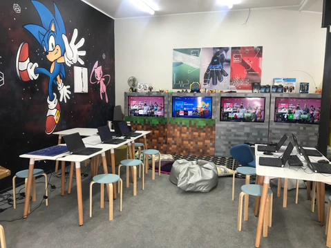 Gaming themed room with characters painted on the wall. 4 screents and a bunch of laptops setup.